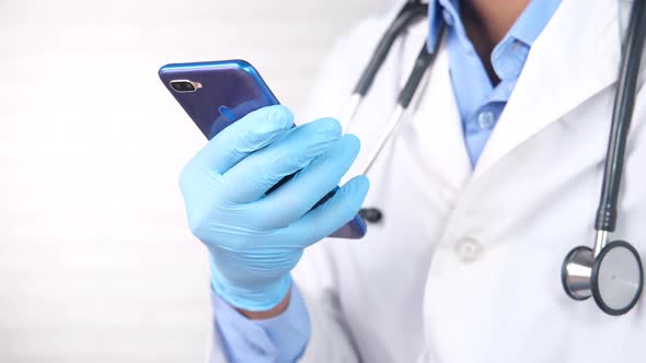 Doctor's Hand in Protective Gloves Using a Smartphone