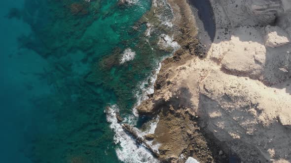 Aerial top down forward over ocean waves crashing on rocky coast. Porto dos Frades, Madeira