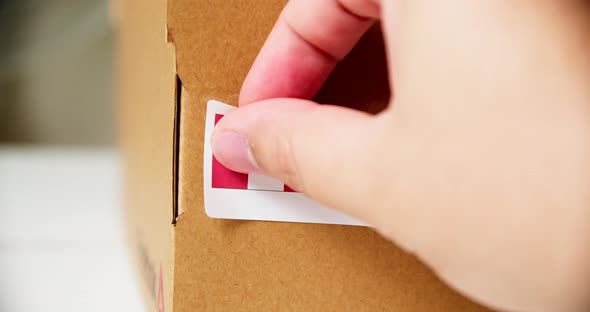 Hands applying MADE IN PERU flag label on a shipping cardboard box with products. Close up shot with