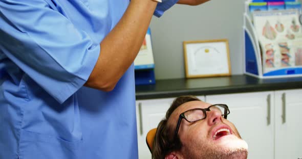 Smiling dentist assistant adjusting dental light over patients mouth