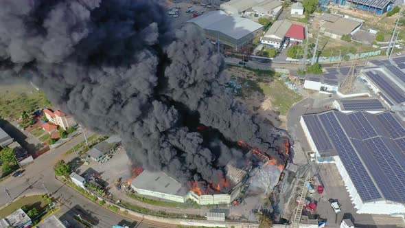 Aerial shot over burning warehouse caused by explosion, black cloud of smoke rising