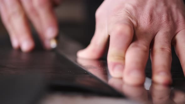 The Tanner Is Cutting Black Leather Sheet with a Razor and Metre