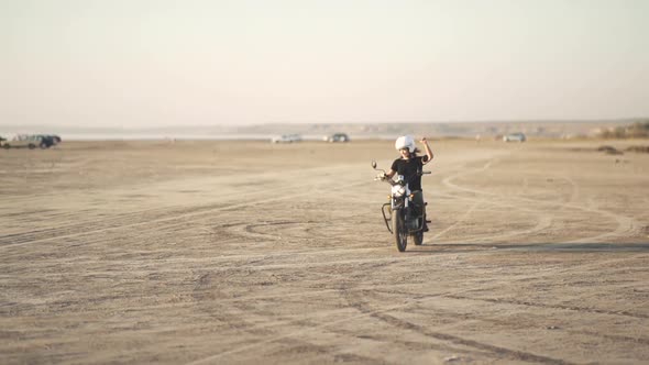 Beautiful Young Woman Riding an Old Cafe Racer Motorcycle on Desert at Sunset or Sunrise