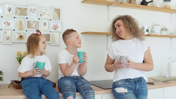 Boy Girl and Mother Drinking a Drink From Blue Mugs Sitting on the Table in a Stylish White Modern