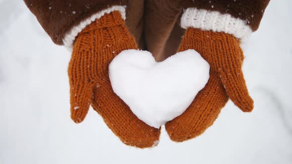 Closeup Of Girl Hands In Ginger Knitted Mittens Holding Heart Of Snow In Winter