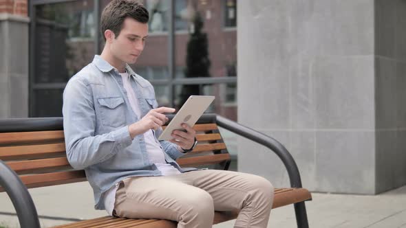 Casual Young Man Sitting Outdoor and Using Tablet