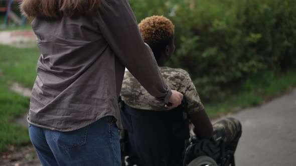 Tracking Shot of Young Caucasian Girlfriend Pushing Wheelchair with African American Boyfriend in