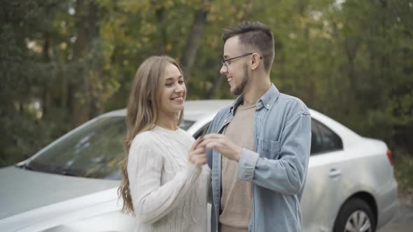 Handsome Young Boyfriend Giving Car Keys To Excited Girlfriend Outdoors