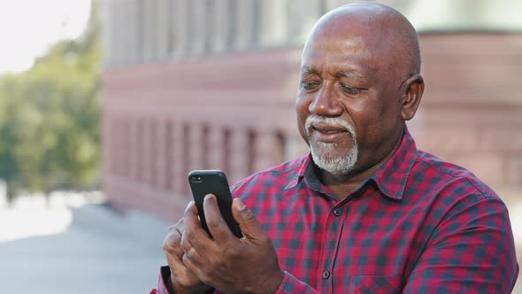 Smiling Focused Senior Black Grandfather Typing Sms Message Looking at Smartphone Screen African