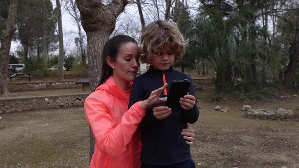 Smiling sportswoman with son on smartphone outdoors