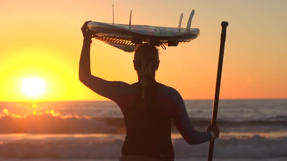 A silhouetted portrait of woman sup stand-up paddleboard surfing at the beach at sunset