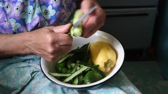 Senior Woman Peel Cucumber with Knife in Her Wrinkled Hands and Cut Raw Vegetable Into Two Part