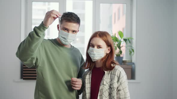 Couple in Medical Masks Stands in an Empty Apartment and Shows the Key to the Camera