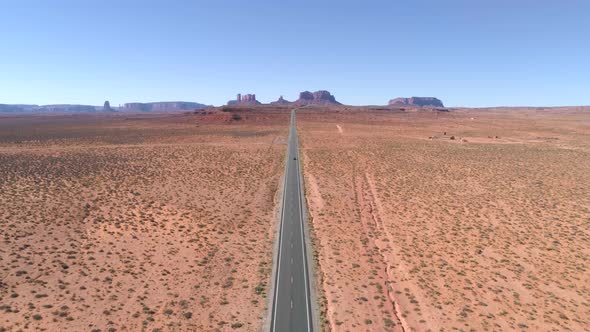 Lonely Car Driving Along an Empty Straight Road Leading Towards Iconic Mountains in Monument Valley