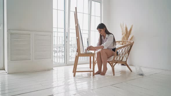 Barefoot Woman Works with Paints on Wooden Easel in Studio