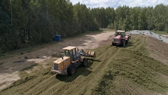 Drone view of tractors tamp the silage in the Silo Trench next to the forest 05