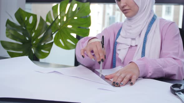 Small Business and Hobby Concept. Muslim Woman Fashion Designer Pinning Paper Pattern at the Table