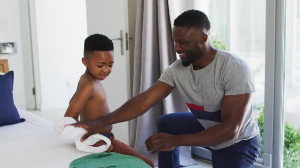 African american father helping his son with getting dressed in bedroom