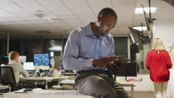 Thoughtful professional businessman using a digital tablet while sitting on his desk in modern offic