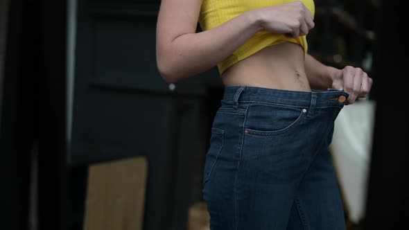 Jeans fit loosely on a thinner woman, close up. Woman looks an mirror