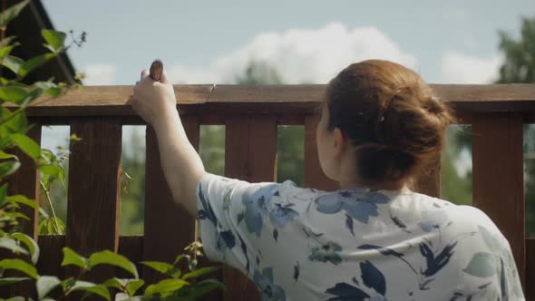 Girl with Red Hair Paints a Wooden Fence with a Brush.