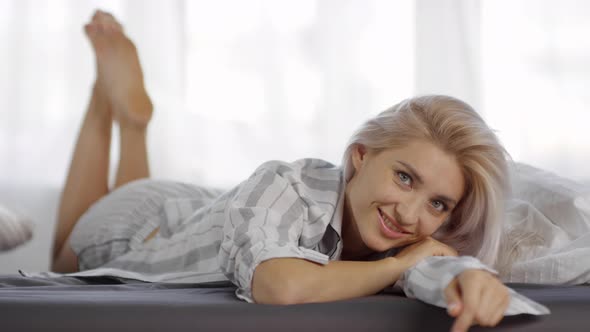 Caucasian Blonde with Seductive Gaze Lying on Bed in Pajamas