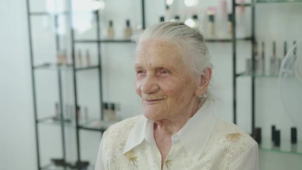 Portrait of Cute Grandmother Smiles and Looks During Makeup Process in Studio