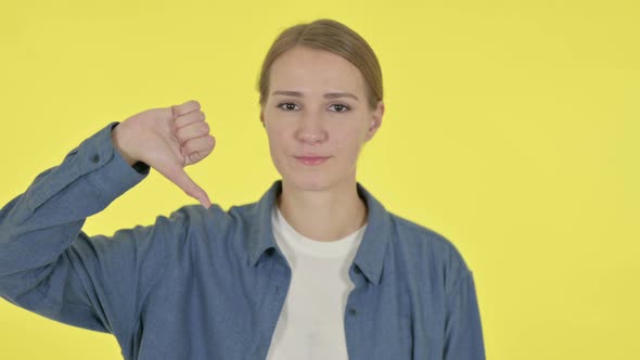 Thumbs Down Gesture By Young Woman on Yellow Background