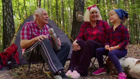 Senior Grandmother Grandfather Granddaughter Telling Funny Stories Fairy Tales Over Campfire in Wood