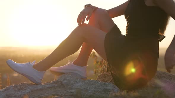 Closeup of Young Elegant Female Slim Legs in Black Short Dress Sitting on a Rock Relaxing Outdoors