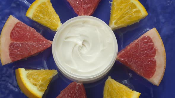 Water Flowing Around Jar of Beauty Cream and Citrus Slices on Blue Background