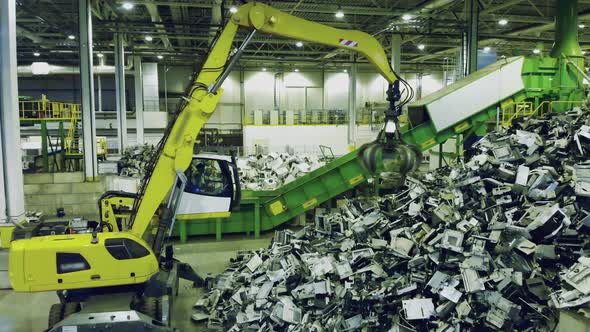 Trash, E-waste, Electronic Garbage Recycling Factory. Excavator Grabs Garbage and Puts It Onto