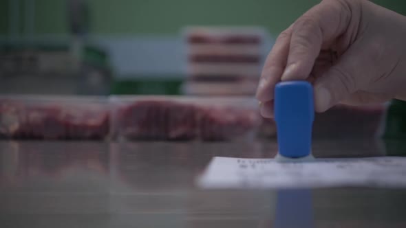 Hands of Worker Puts Stamp on the Labels for Marking Trays with Different Cuts of Fresh Raw Beef