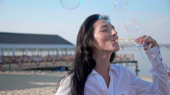 Pretty Woman Blowing Soap Bubbles on the Beach with a Sea on Background  Slow Motion