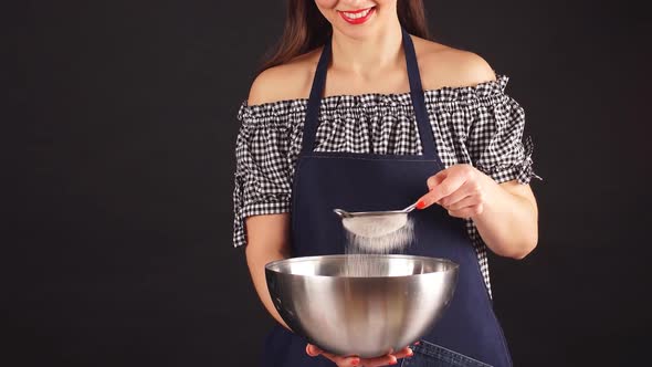 Charming Female Confectioner Sift the Flour on a Dark Background