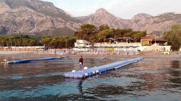 Aerial View of a Pensive Young Girl Standing on the Plastic Floating Pier in the Sea Against the