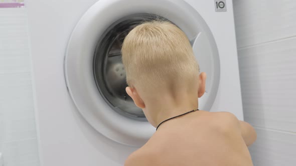 A Cute Boy Is Watching the Washing Machine at Home.