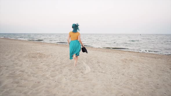 Pretty Woman with Dyed Blue Hair Runs Near Sea or Ocean, Enjoying Freedom During Summer Holidays