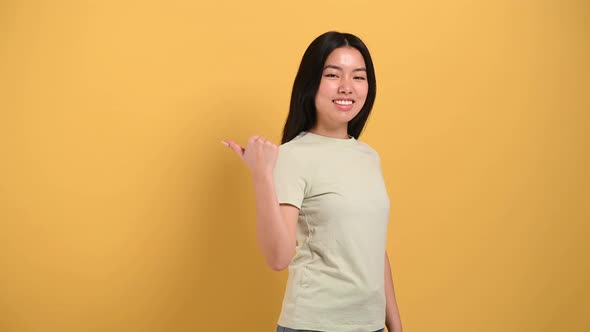 Happy Lovely Millennial Brunette Longhaired Asian Young Woman Points with Hands to Empty Space to