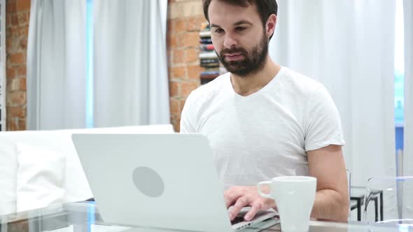 Beard Man Drinking Coffee From Cup and Working on Laptop