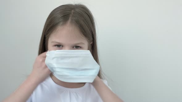 Little Girl Puts on a Preventive Medical Face Mask and Giving Thumbs Up on Gray Background with Copy