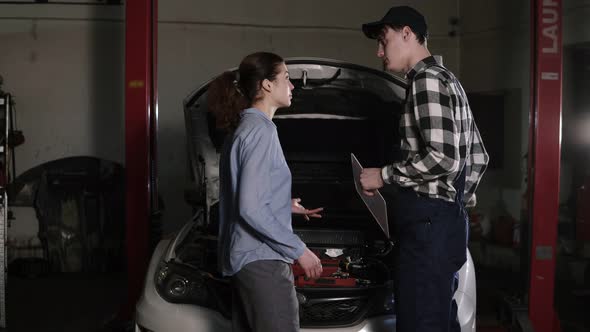 Cute Car or Automotive Technician Wearing Work Robe and a Cap is Meeting with His Female Clients and