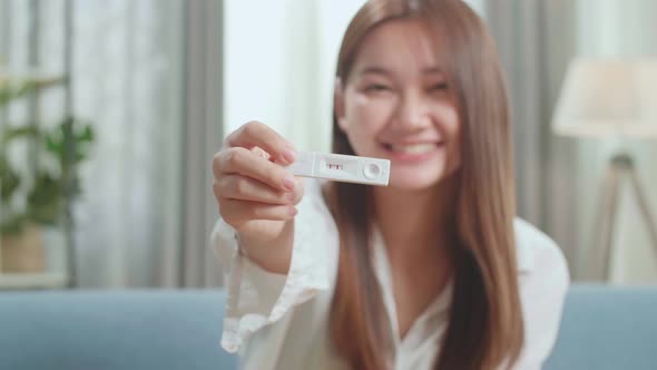 Happy Young Asian Woman Holding Pregnancy Test And Warmly Smiles To Camera