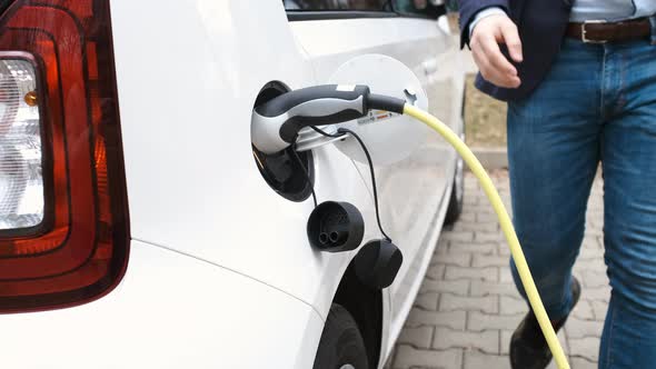 Man Coming to the Electric Car and Unplugging Charging Cable