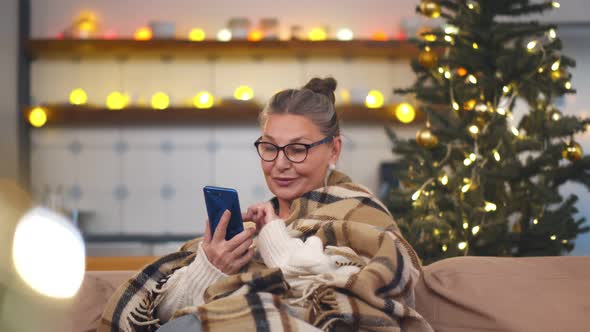 Senior Woman Sitting on Sofa with Smartphone at Christmas Time