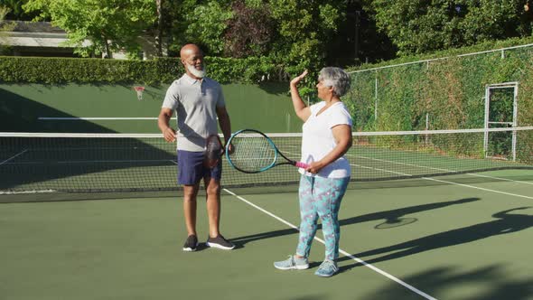 African american senior couple holding rackets high fiving each other on the tennis court