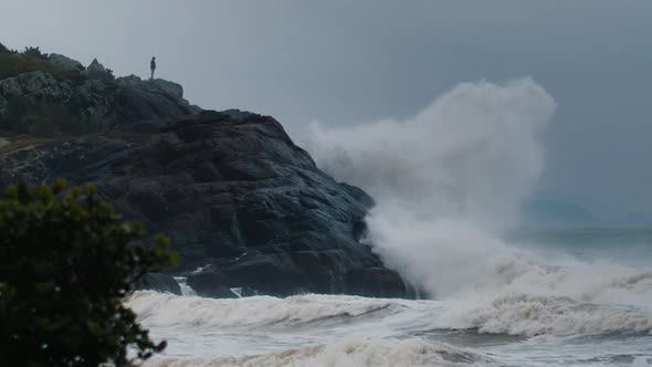 Man Stands on the Rock and Watches Huge Waves Breaking Over the Rock During Storm in the Ocean