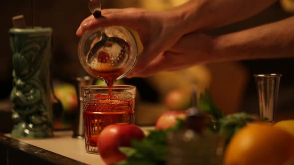 The Bartender Pours an Alcoholic Drink Into a Glass with Ice in a Thin Stream