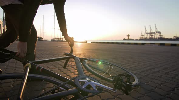 Young Hipster Man Walking with Bicycle During Sunset or Sunrise with Sea Port on Background