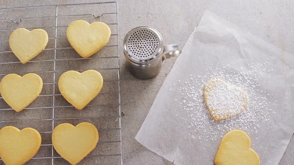 Raw heart shape cookies on baking tray with flour shaker strainer and wax paper